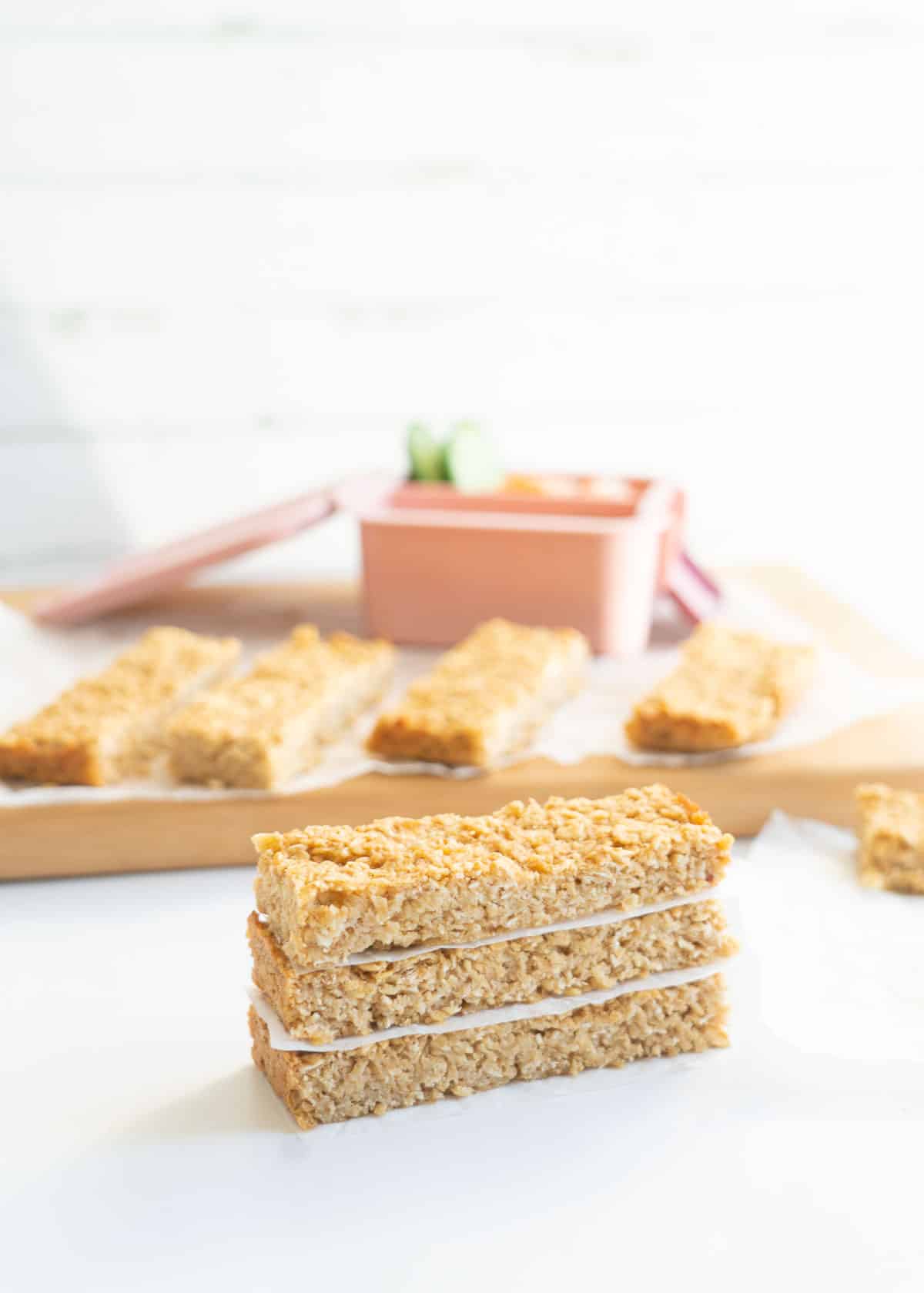 A stack of three oat bars on a white bench top in front of a wooden chopping board.