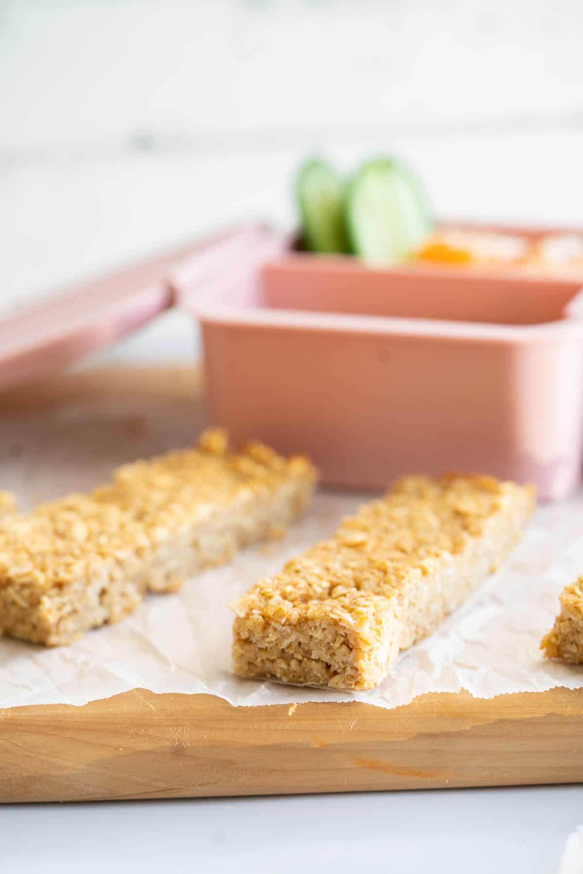 An oatmeal bar on a wooden chopping board with a pink lunchbox in the background.