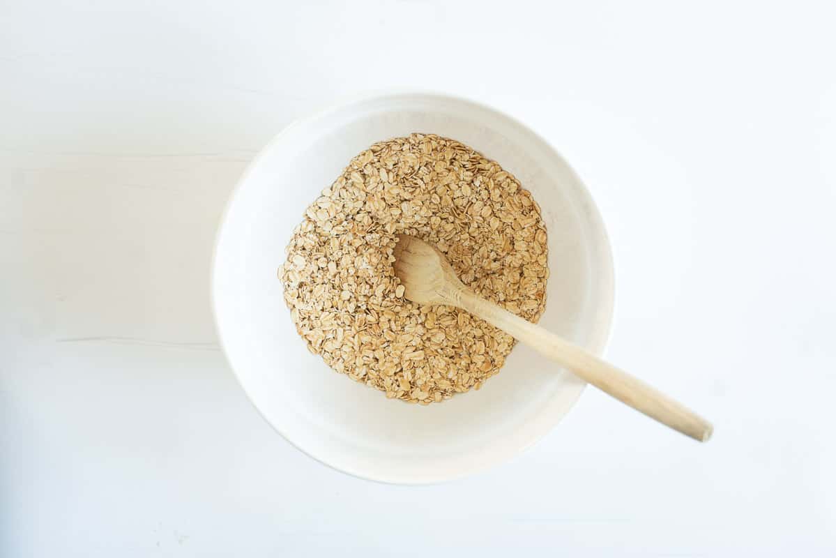 A white ceramic mixing bowl containing rolled oats and cinnamon.