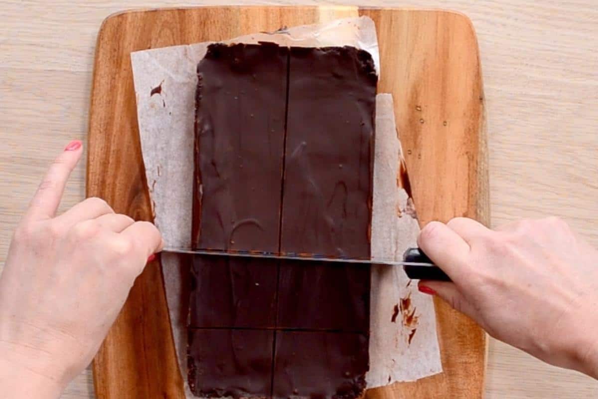 Chocolate weetbix slice on a wooden chopping board being cut into pieces.