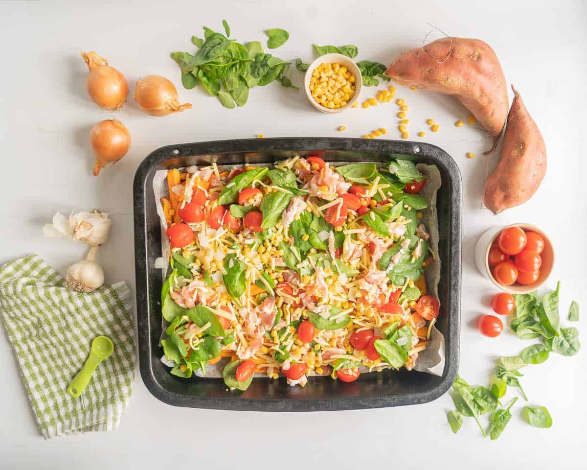 Sweet potato topped with colourful vegetables, chopped bacon and grated cheese ready to go into the oven to bake.