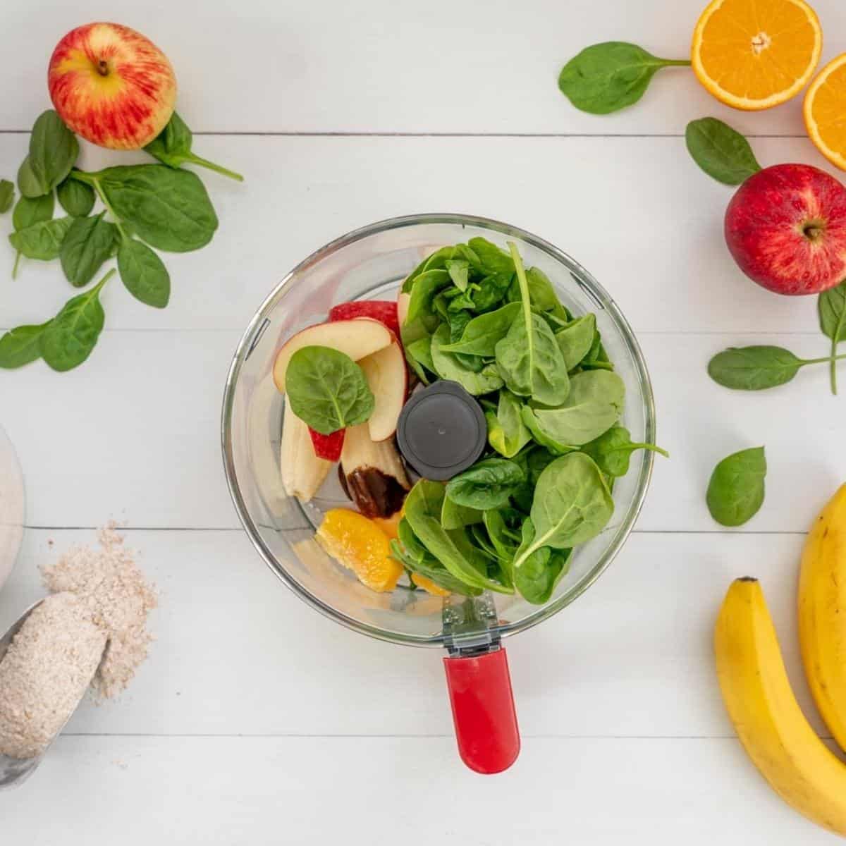 Spinach leaves, orange and apple in a food processor ready to be blended.