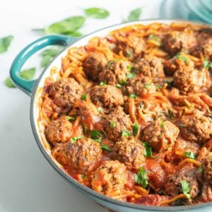 A large green casserole dish fillined with meatballs, pasta and marinara sauce.