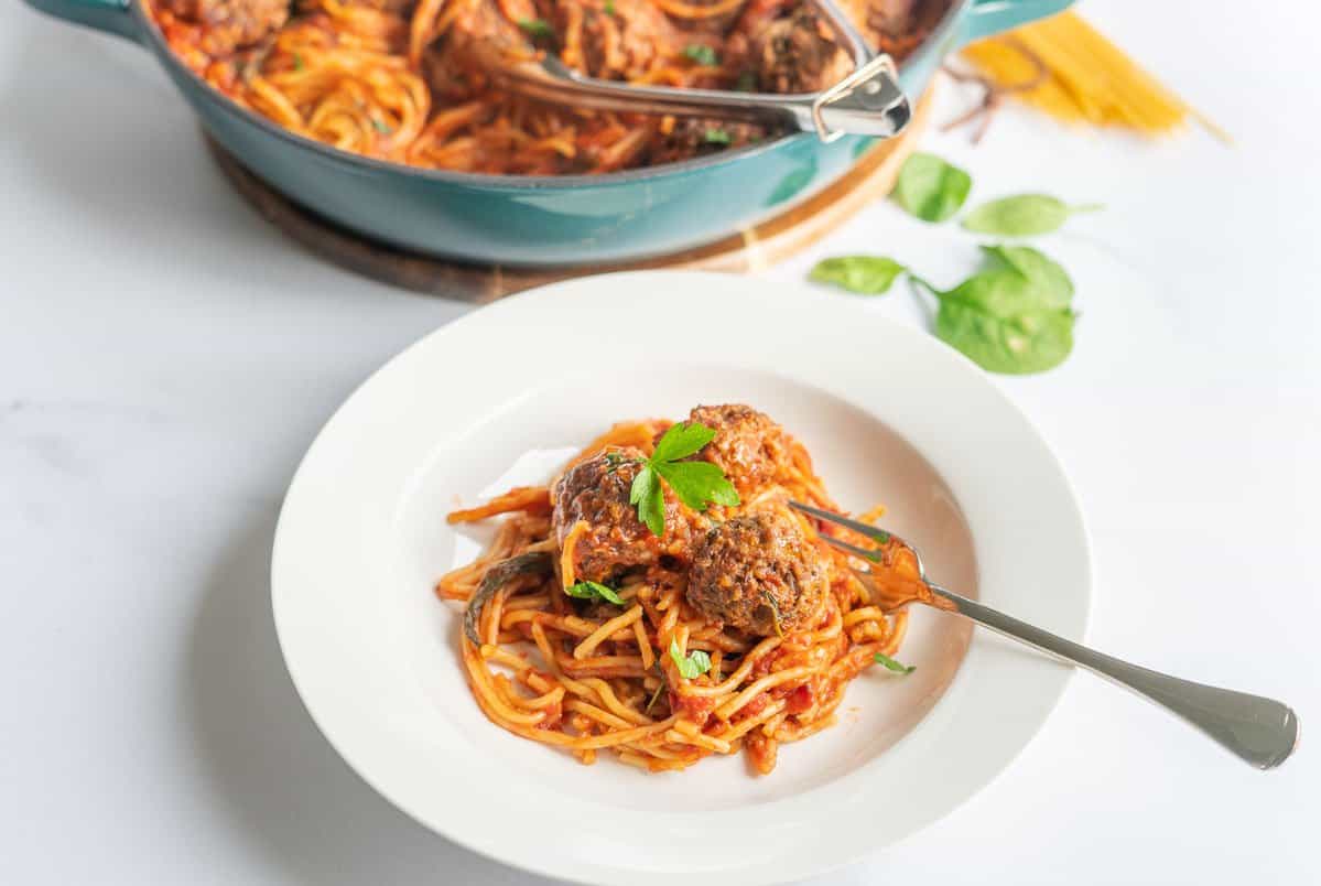 A white bowl of spaghetti and sauce topped with meatballs.