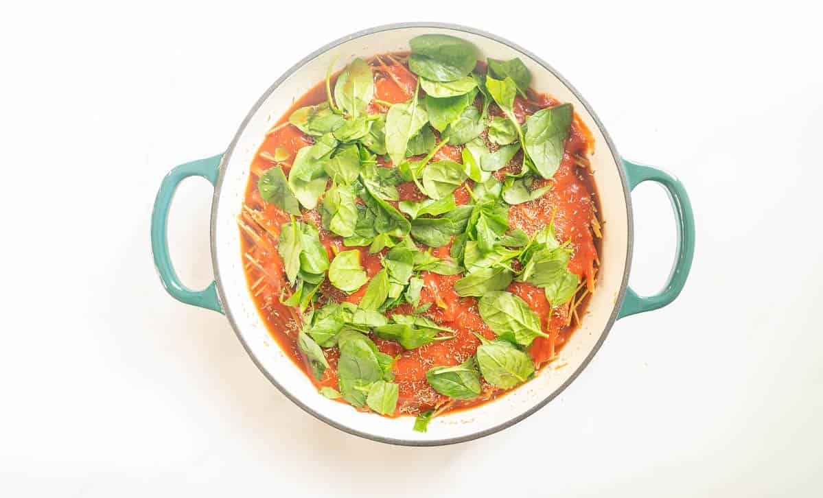Tomato puree topped with herbs and spinach leaves in a large casserole dish.