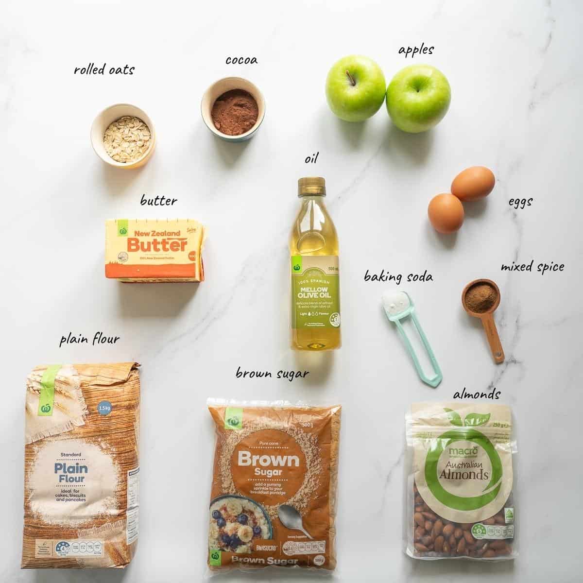 Ingredients to make a chocolate apple cake with crumb topping laid out on a bench top with text overlay.