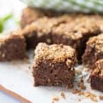 A piece of chocoalte apple cake with crumble topping on a piece of baking paper.