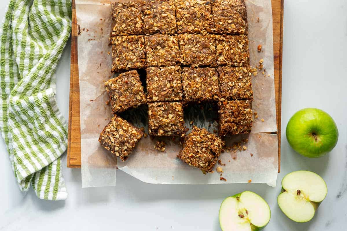 Pieces of chocolate apple cake on a wooden chopping board, next to a green checked tea towel and green apples.