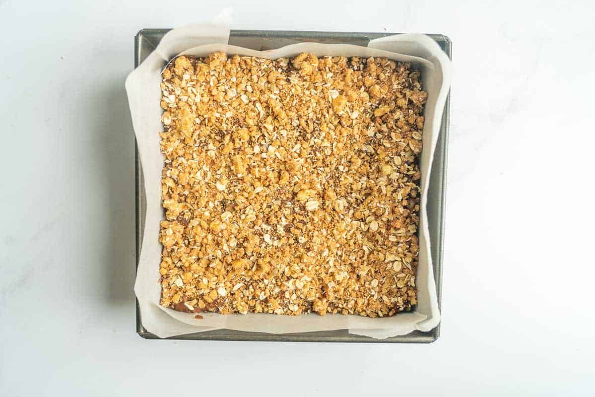 Chocolate apple cake batter topped with a crumb topping in a lined cake tin.