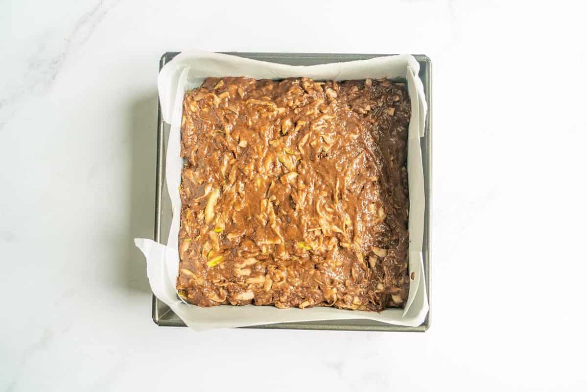 Chocolate apple cake batter in a lined square baking tin.