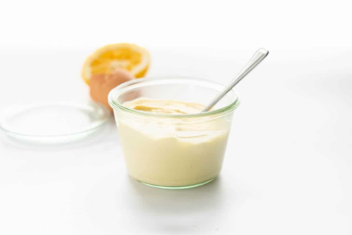 A glass jar filled with mayonnaise with a spoon, sitting next to the lid of the jar.