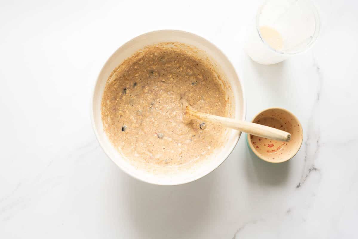 Thick waffle batter with blueberries in a mixing bowl with a wooden spoon.