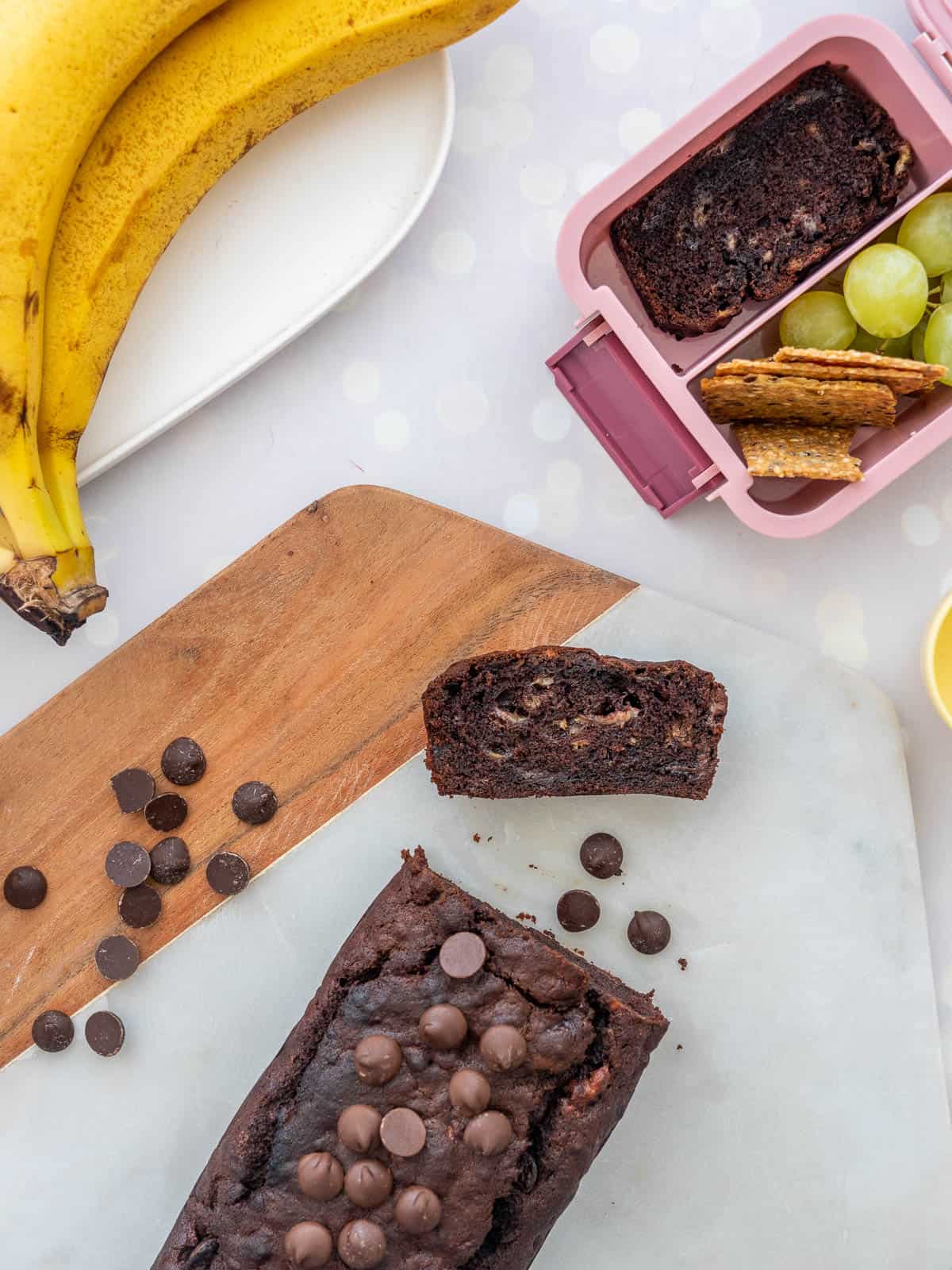 A chocolate loaf on a hexagonal marble board, with a slice packed into a small pink lunchbox.