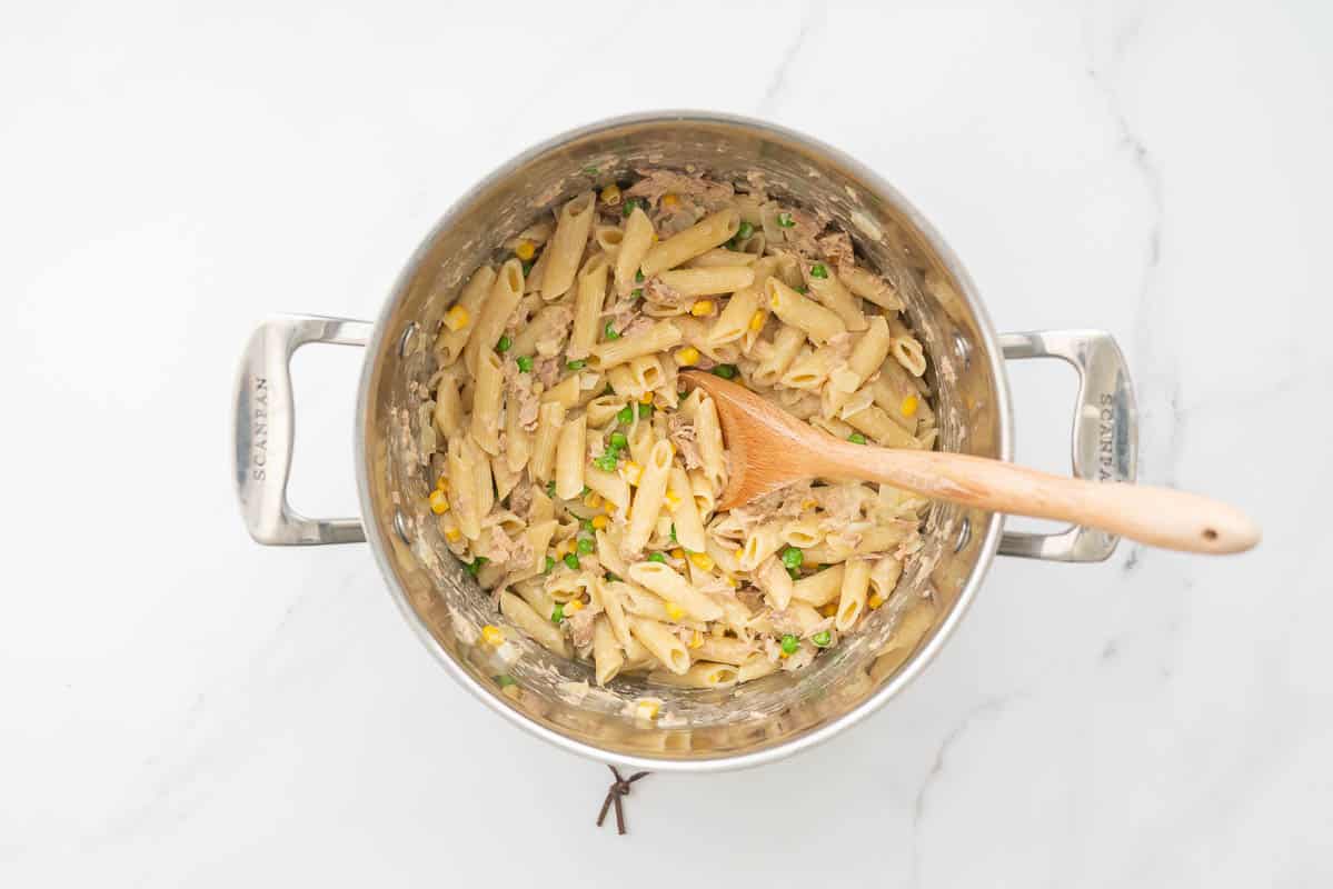 A large sauce pan containing pasta, a creamy tuna sauce, peas and corn.