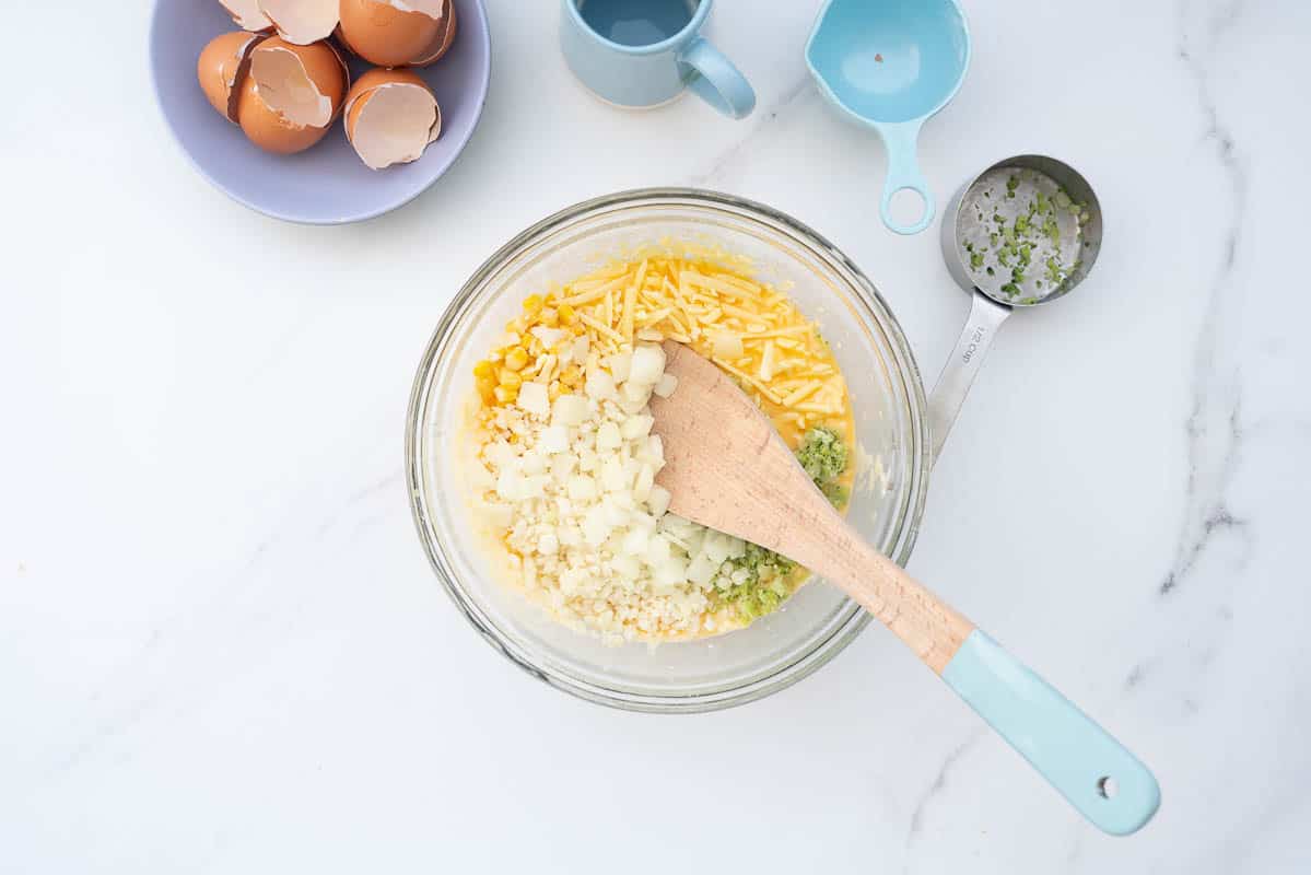 A mixing bow containing an egg batter with chopped vegetables and grated cheese.