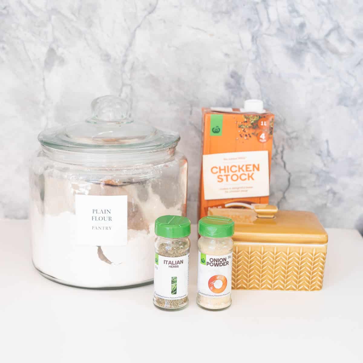 Chicken gravy ingredients: flour, stock, butter, herbs and onion powder sitting on a bench top.