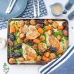A roast chicken tray bake on a table set with blue placemats, plates, cutlery and a gravy boat.