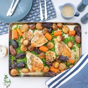 A roast chicken tray bake on a table set with blue placemats, plates, cutlery and a gravy boat.