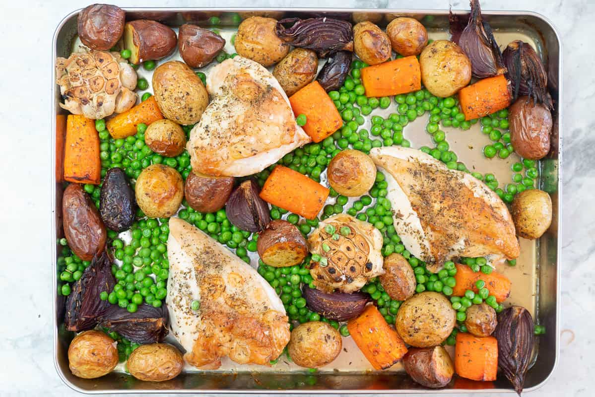 Roasted chicken breasts with crispy skin, roast vegetables and peas in a roasting tray.