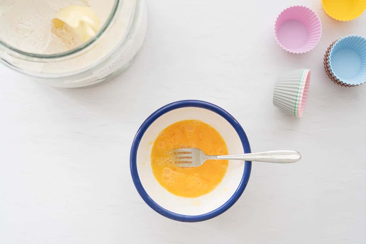 Whisked eggs in a blue rimmed white enamel bowl.