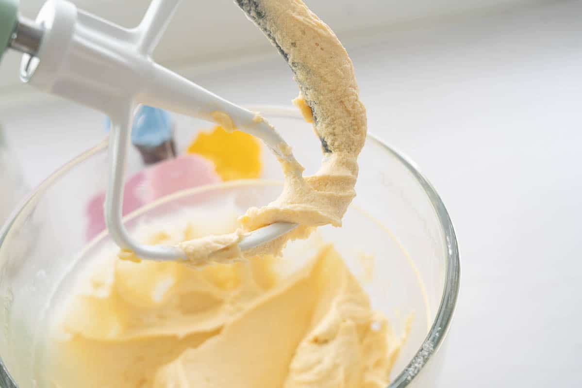Vanilla cupcake batter on the beater attachment of a stand mixer.