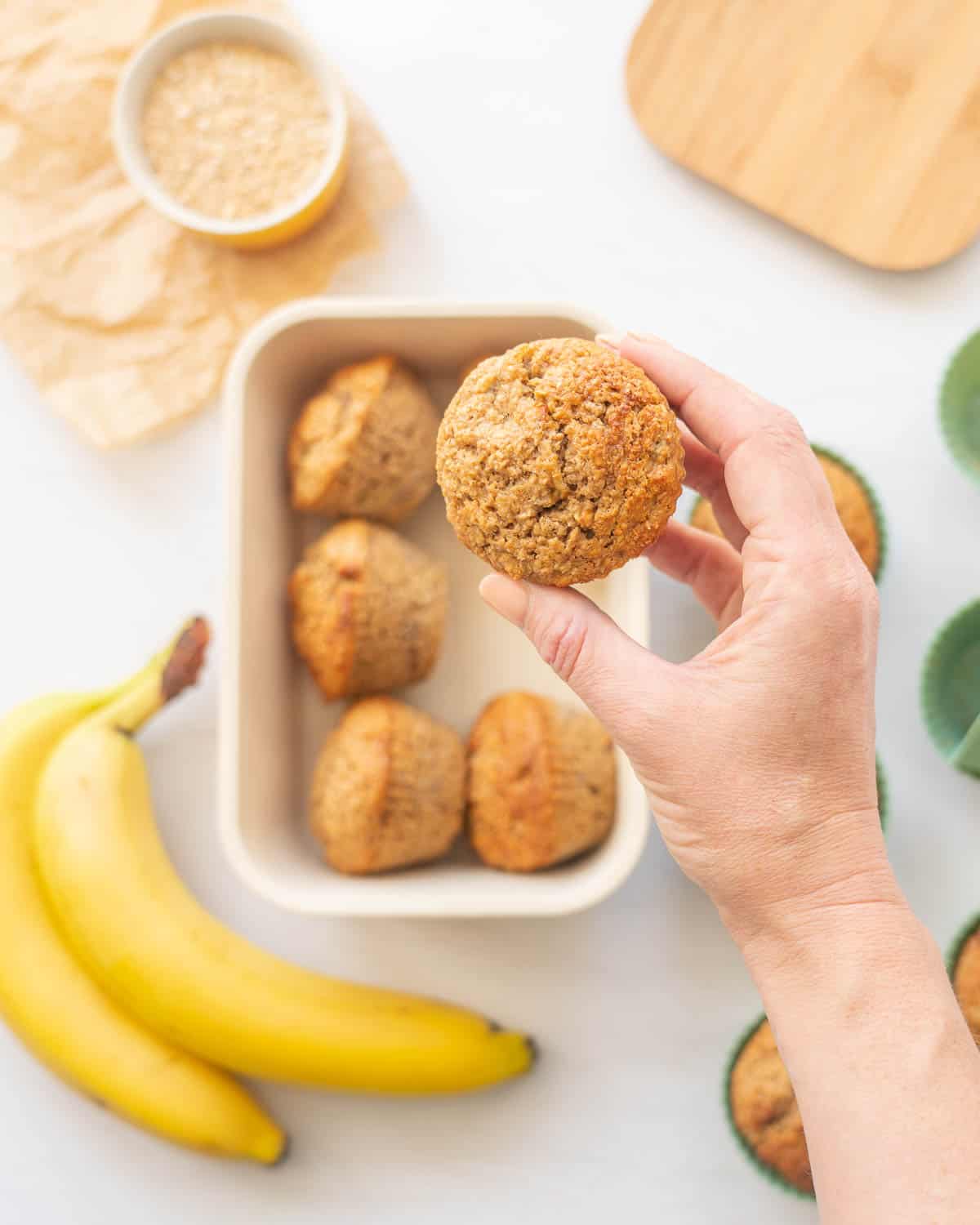 A muffin being held above a box of muffins.