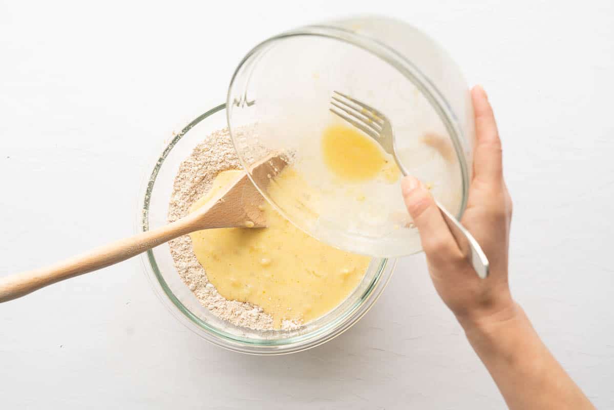 Wet ingredients being poured into dry ingredients to make a bran muffin batter.