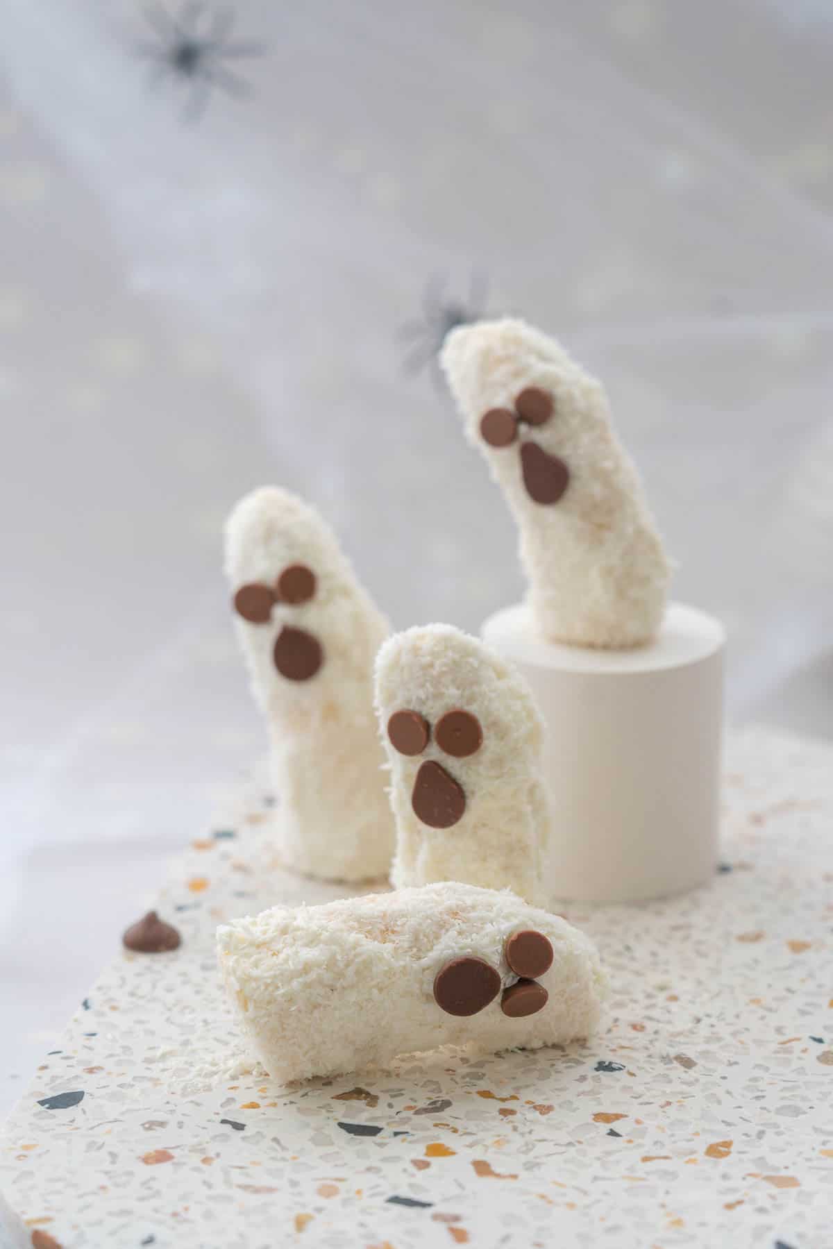 Foour banana halves decorated to look like ghosts for halloween on.a terrazzo platter