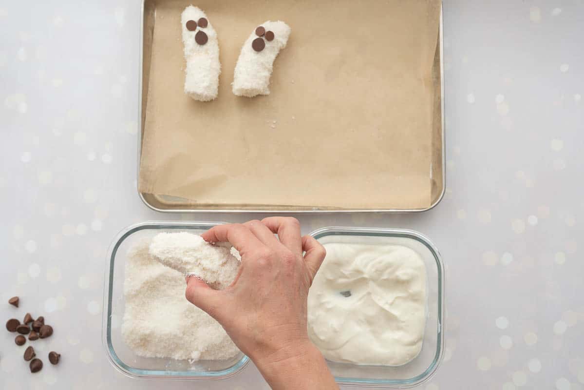 A yoghurt dipped banana being rolled in desiccated coconut.