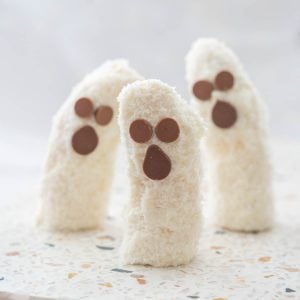 3 banana halves standing upright on a terrazzo platter decorated to look like ghosts.
