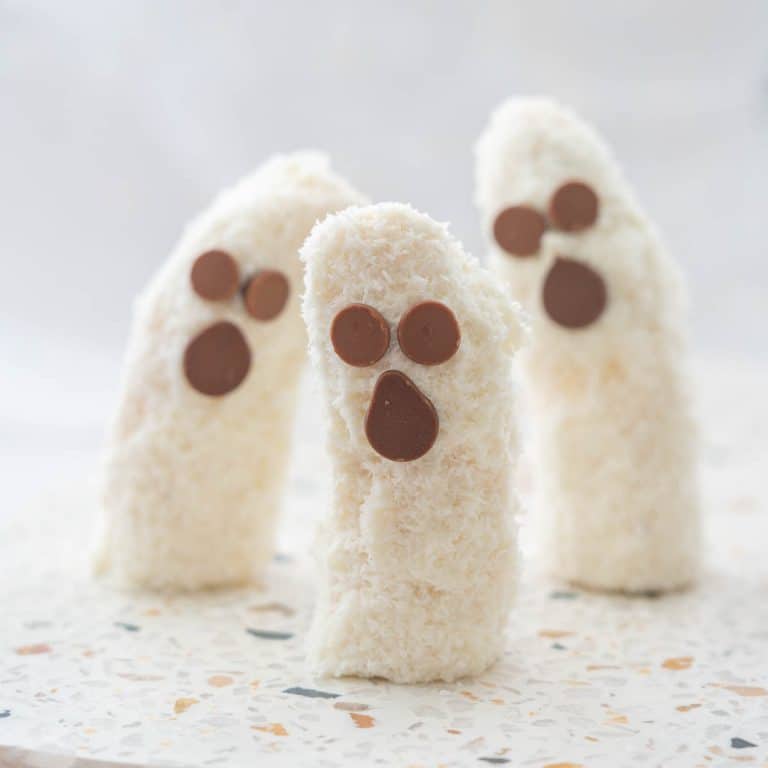 3 banana halves standing upright on a terrazzo platter decorated to look like ghosts.
