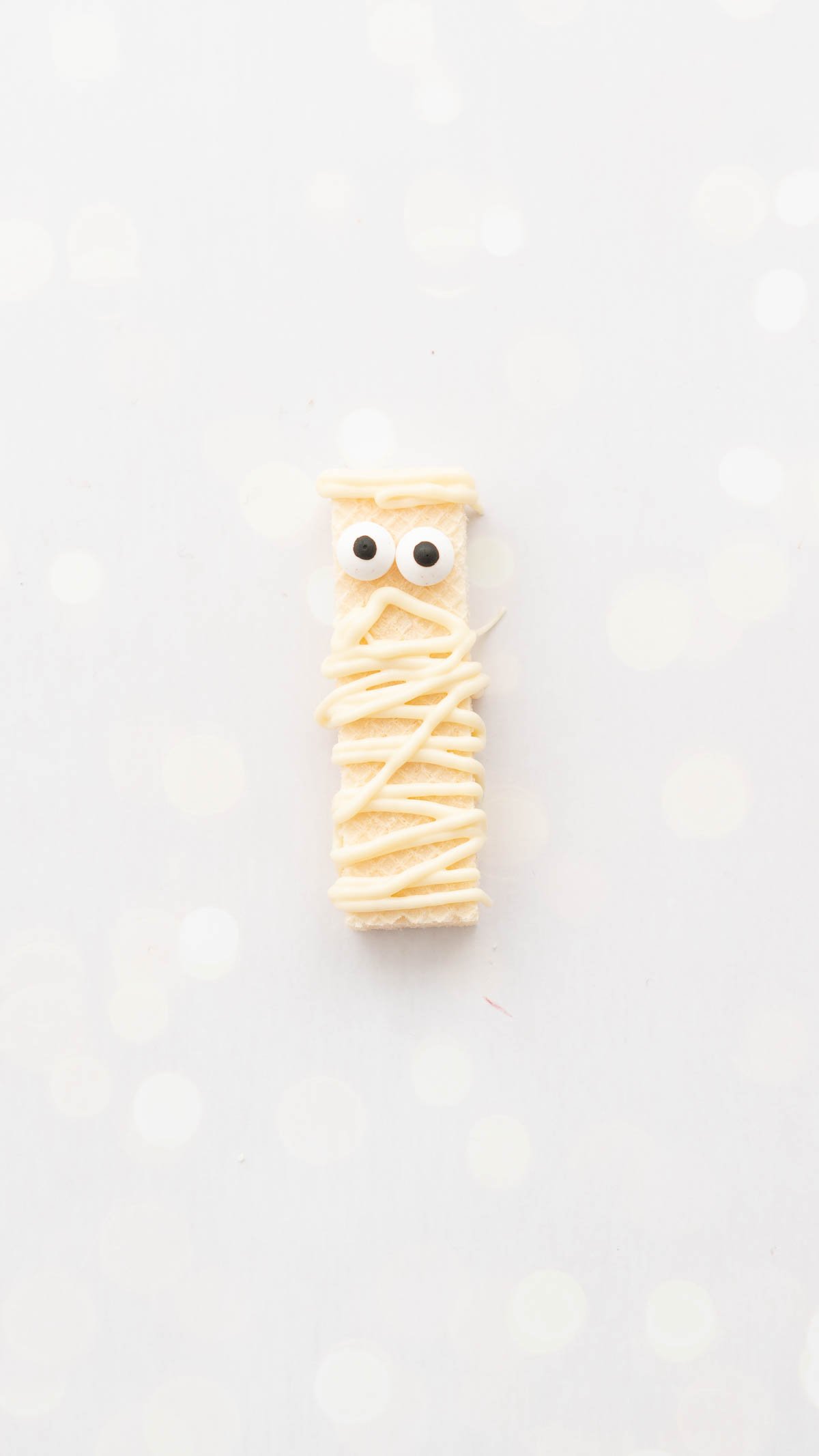 A cookie decorated as a mummy sitting on a bench top.