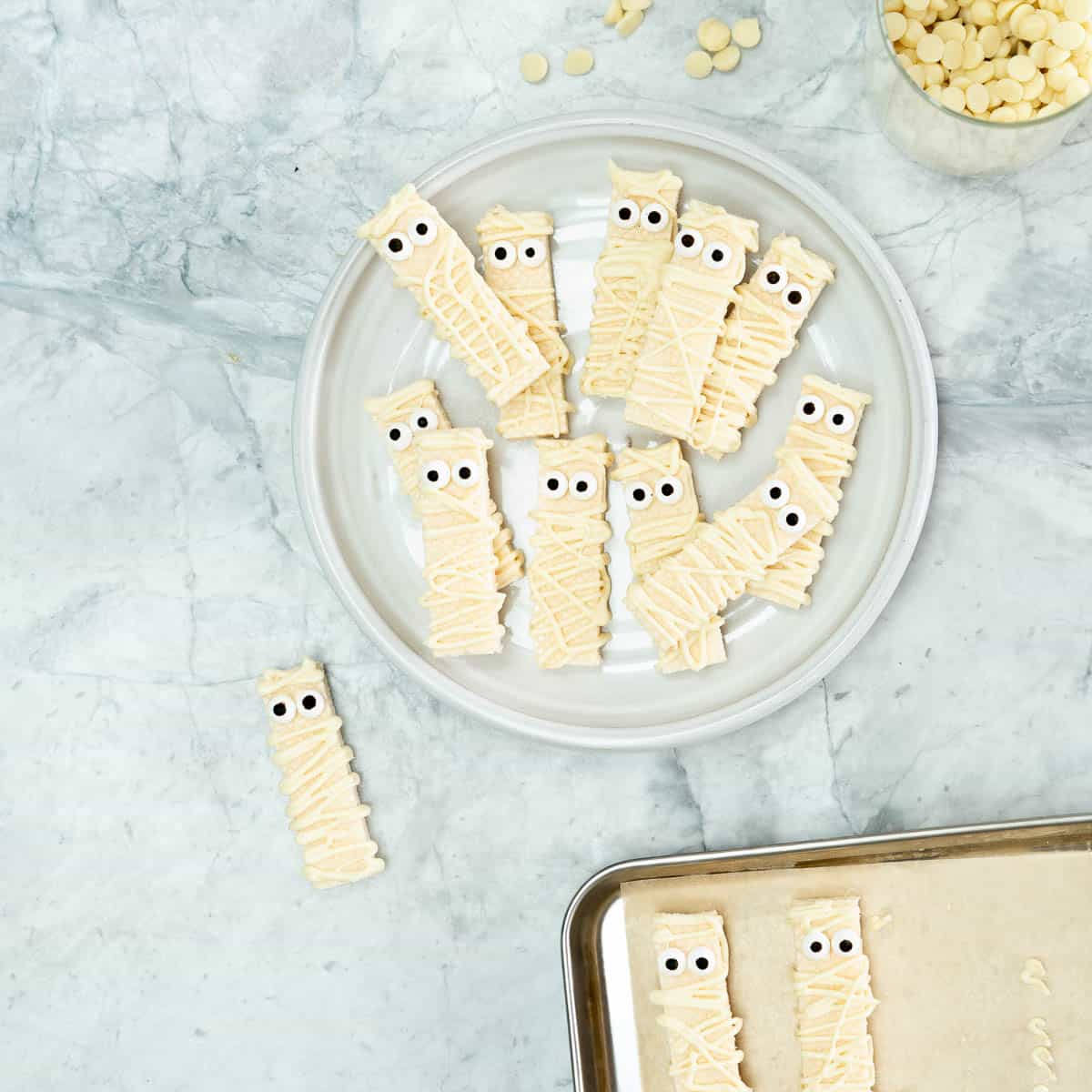 Cookes decorated to look like mummies on a white plate sitting on a grey marble bench.