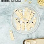 Mummy Cookies decorated for halloween on a white platter on a grey marble bench top, with text overlay for pinterest.