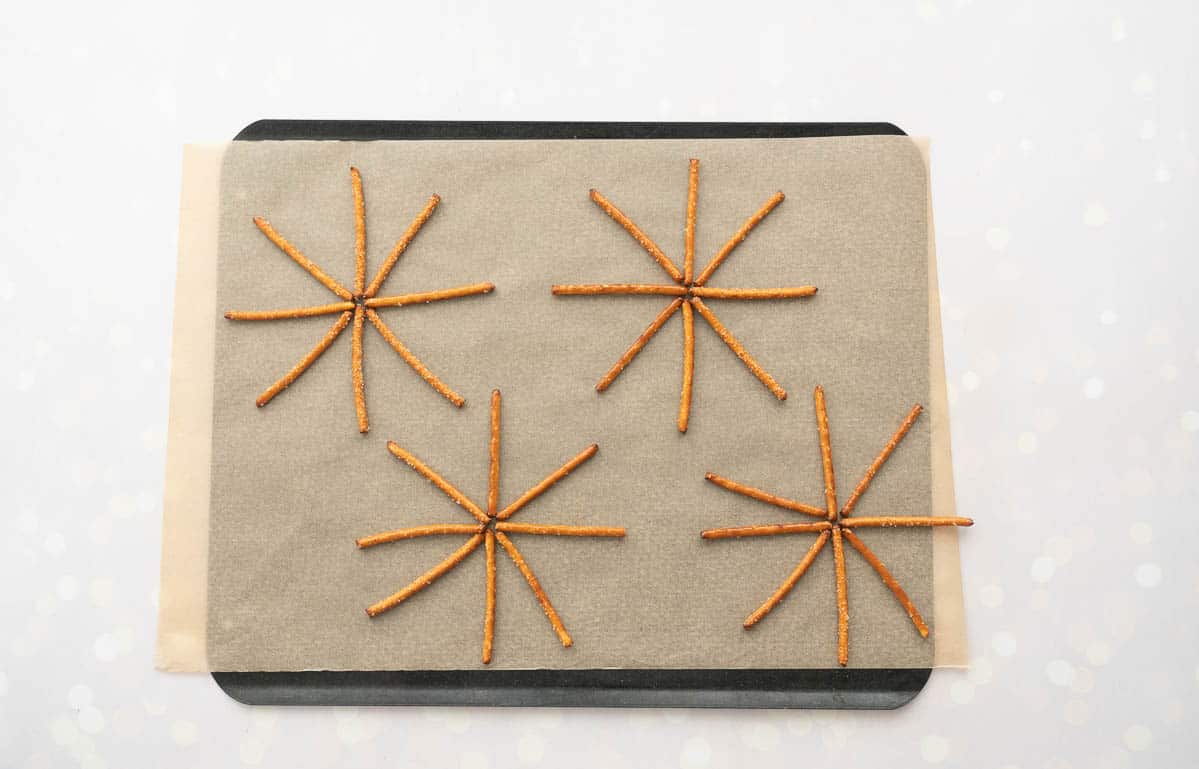 Pretzel sticks lied out in star shapes on a lined baking tray.