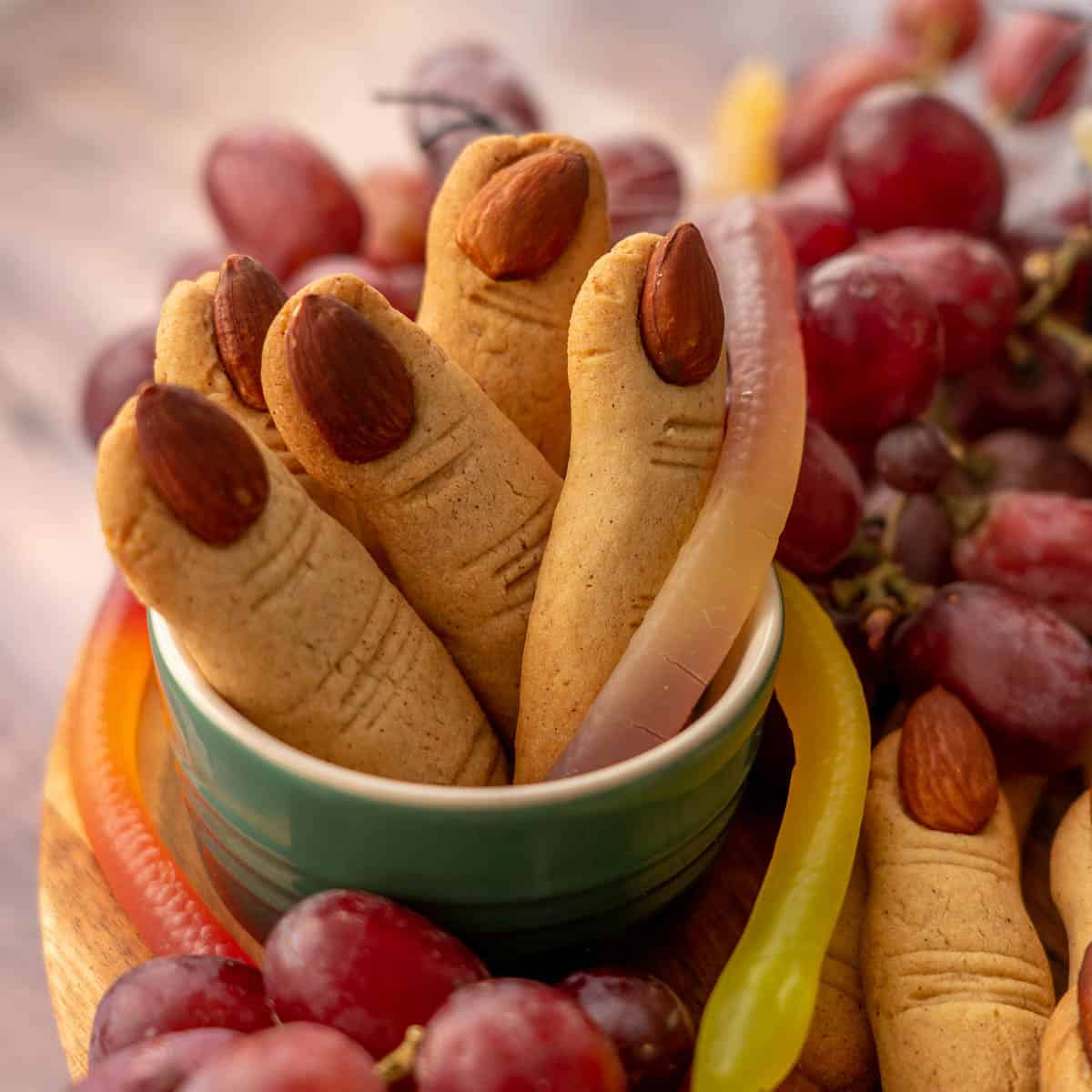 Sugar cookies shaped and decorated to look like witches fingers standing up right in a small dish.