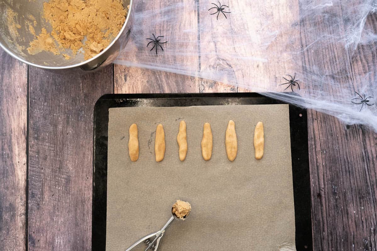 Finger shaped pieces of cookie dough on a lined cookie sheet.