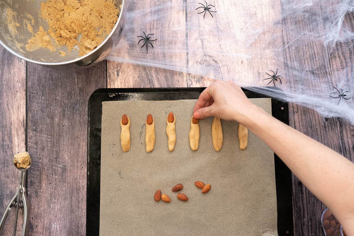 Almonds being pushed into the end of finger cookies to create witch fingernails.