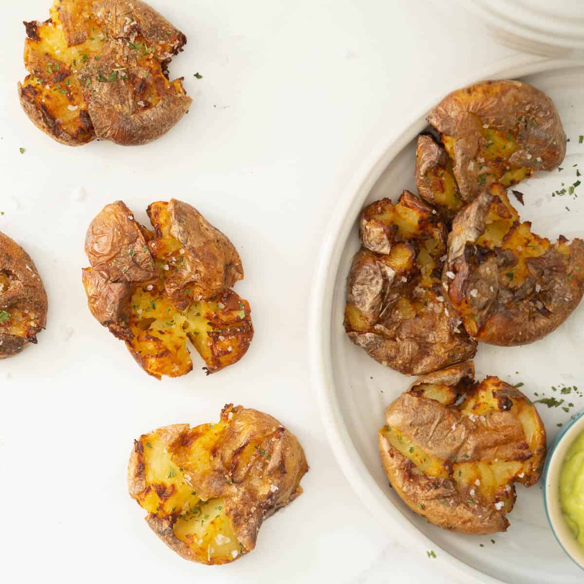 Crispy potatoes sprinkled with parsley and salt flakes sitting on a white bench top