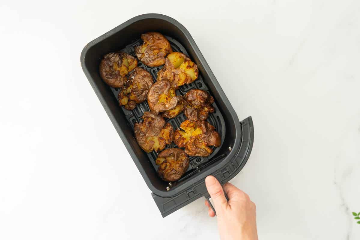 Smashed potatoes cooked to a deep golden brown in an air fryer basket.