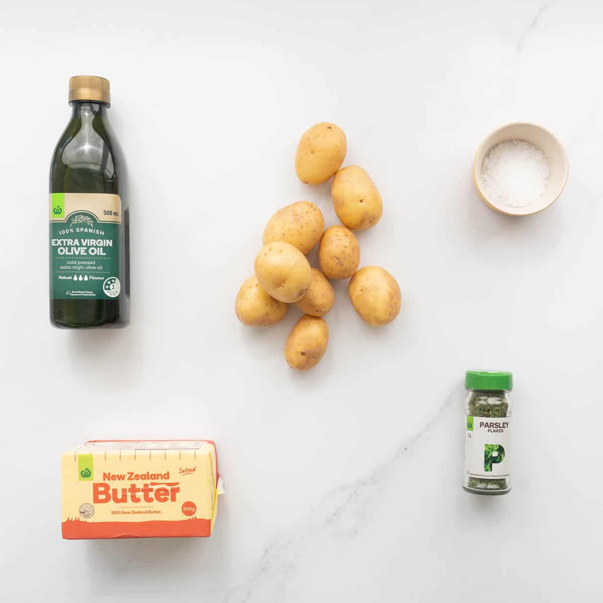 Potatoes, olive oil, butter, salt and parsley lying on a bench top.