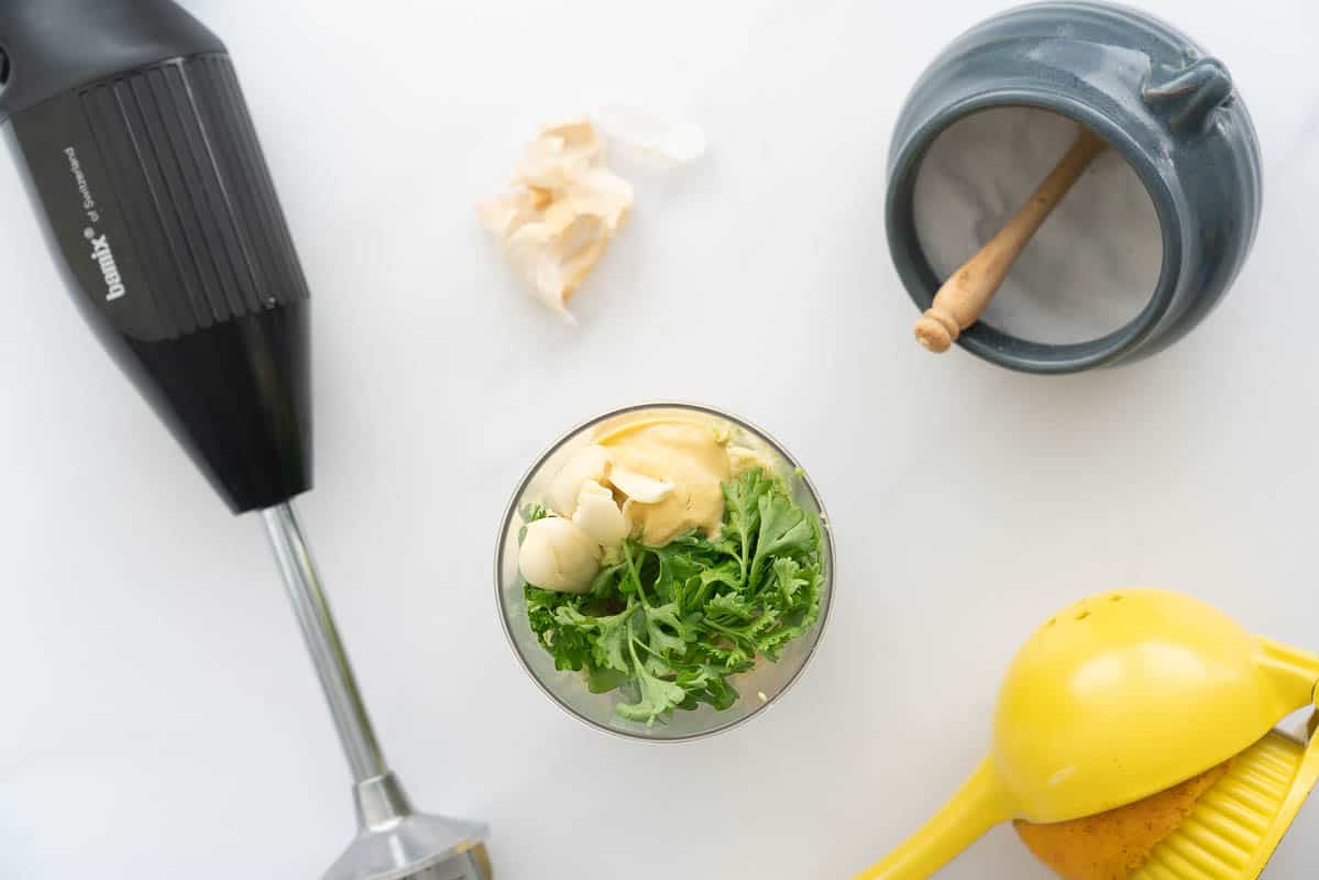 A blender cup filled with garlic cloves, avocado, parsley.