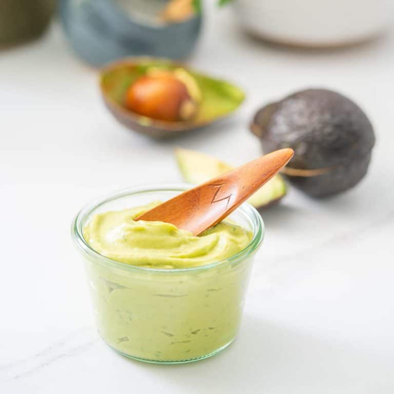 A glass jar filled with creamy avocado with a wooden spoon resting on the surface.
