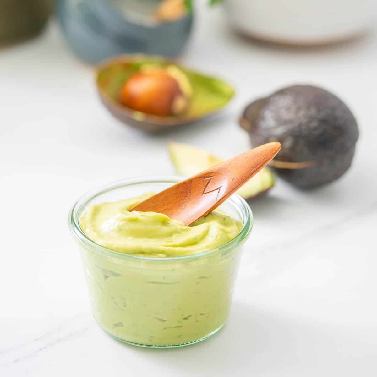 A glass jar filled with creamy avocado being scooped out with a small wooden spoon.