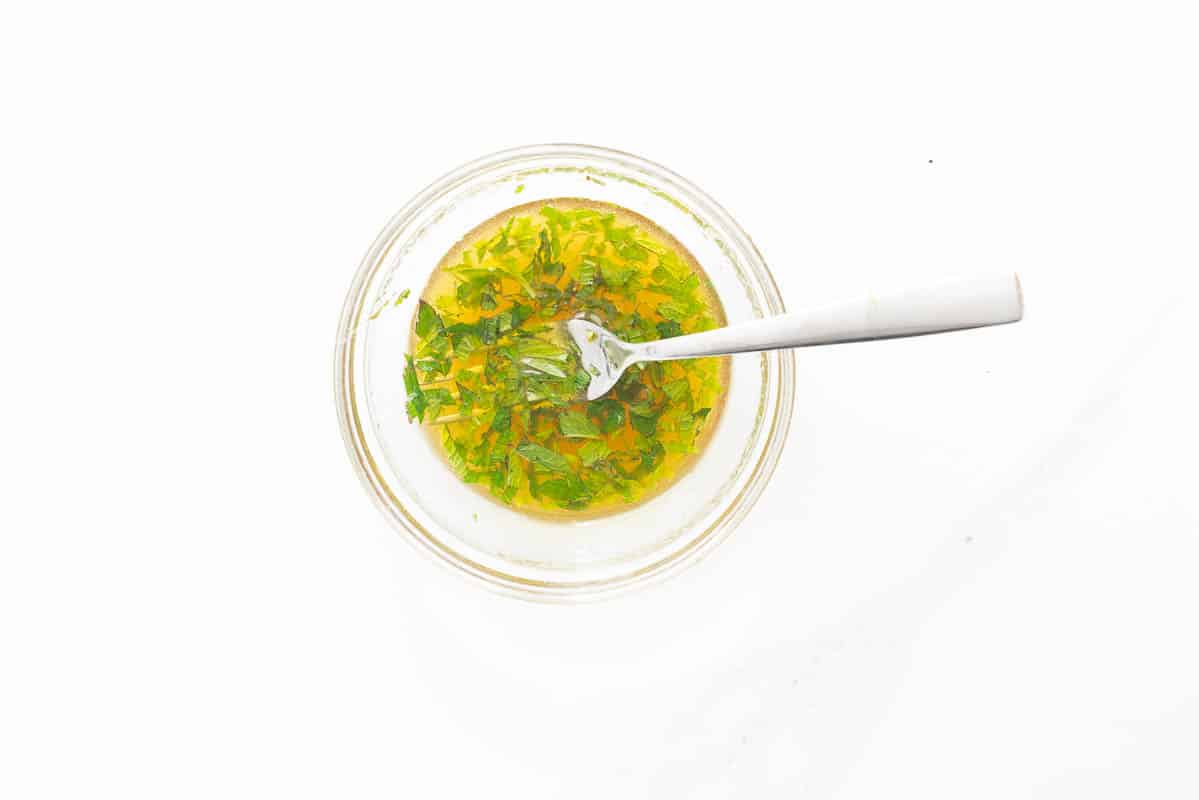 A small glass bowl of honey mint dressing sitting on a white bench top.