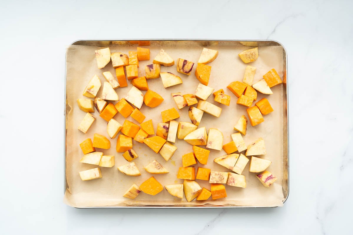 Cubes of orange and gold sweet potato on a lined baking tray.