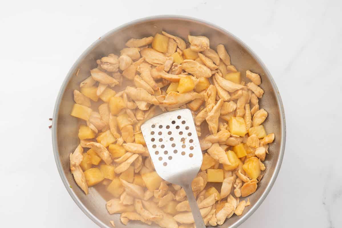 A large stainless steel fry pan of browned chicken, pineapple pieces and hoisin sauce.