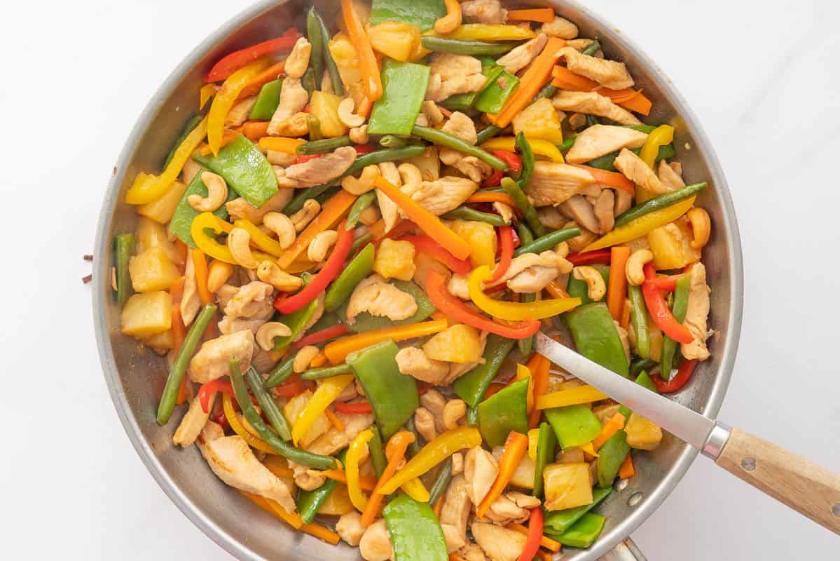 A large stainless steel fry pan of colourful stir fried vegetables, chicken and pineapple.