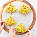 Two children's hands reaching out to pick up 4 triangular pieces of pita bread decorated to look like Christmas trees.