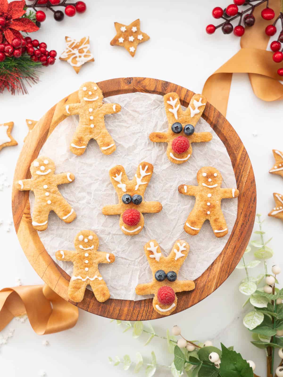 A collection of christmas cookies on a wooden board surrounded by christmas decorations.